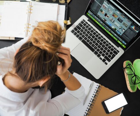 Overhead view of a stressed woman working at a desk with a laptop, phone, and notebooks.