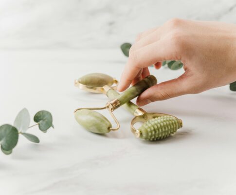 Close-up of a hand holding jade rollers on a marble surface for skincare and wellness.